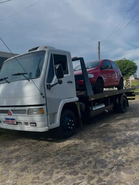 Caminhão guincho plataforma branco com carro vermelho em rua de paralelepípedo em Viamão
