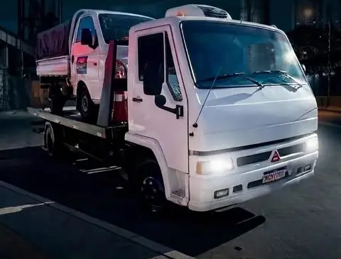 Caminhão guincho plataforma da Na Hora Guinchos com faróis acesos transportando utilitário à noite